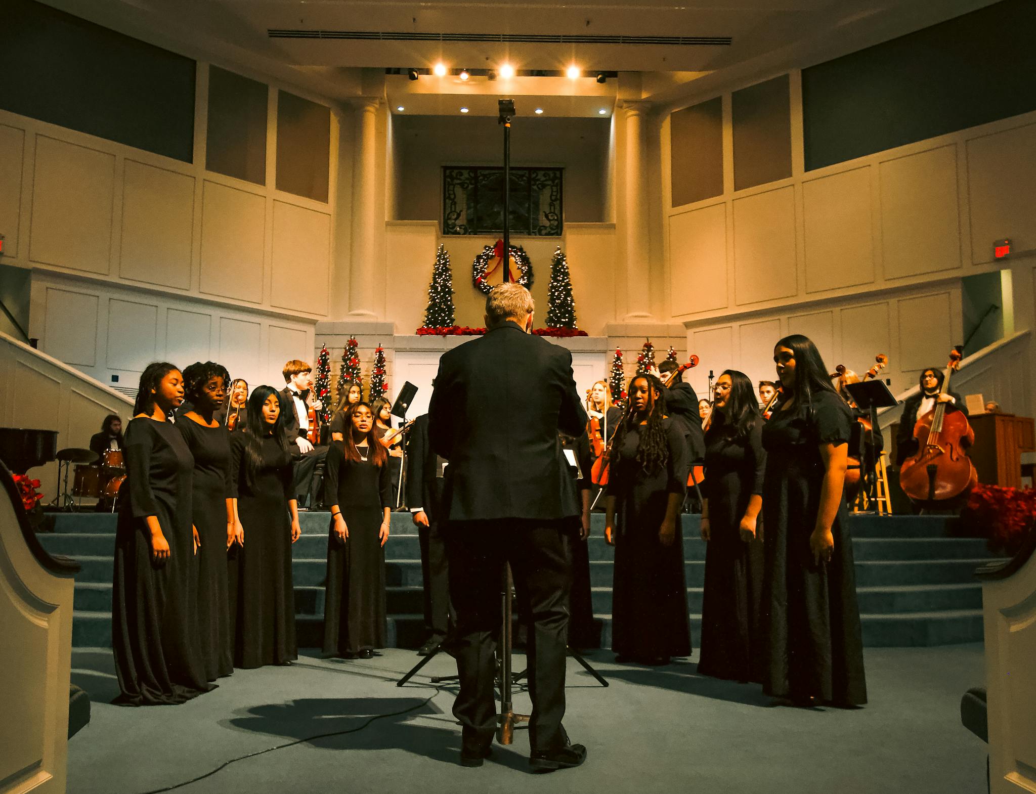 Choir in black attire sings at a church with Christmas decorations.